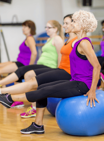 Several women are in an exercise class. They are sitting on exercise balls and have one leg stretched out in front of them. 